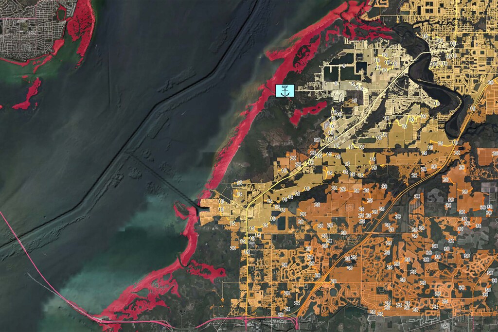 The image shows a map of a coastal area. An area highlighted in red shows where the water is too shallow for safe navigation. Areas in yellow and orange show isochrones that indicate how far a UGV can traverse in a certain amount of time from its current position. 